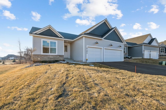 view of front of property featuring board and batten siding, a garage, stone siding, driveway, and a front lawn