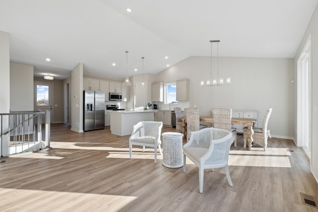 living room with a chandelier, visible vents, vaulted ceiling, and light wood finished floors