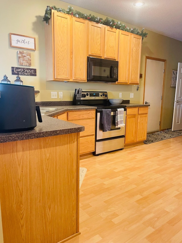 kitchen with light wood finished floors, dark countertops, stainless steel range with electric stovetop, light brown cabinets, and black microwave