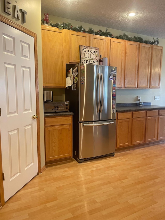 kitchen featuring a textured ceiling, dark countertops, freestanding refrigerator, and light wood-style floors