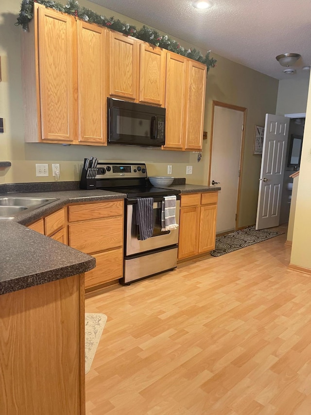 kitchen featuring stainless steel range with electric stovetop, dark countertops, black microwave, and light wood-style floors