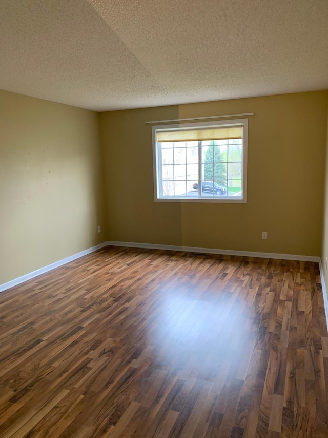 empty room featuring a textured ceiling, dark wood-style flooring, and baseboards