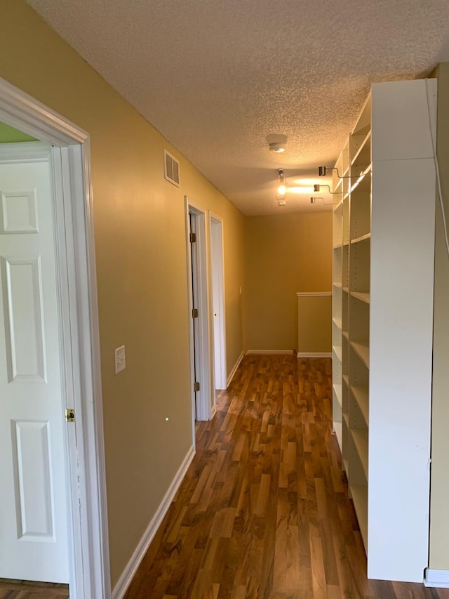 corridor with a textured ceiling, dark wood-type flooring, visible vents, and baseboards