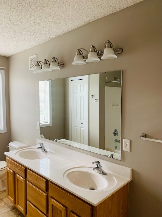 full bath with a sink, a textured ceiling, toilet, and double vanity