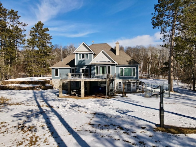 snow covered property featuring stairs, a chimney, and a wooden deck