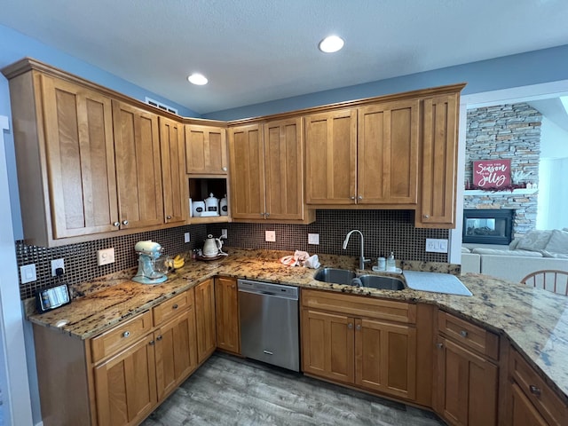 kitchen featuring brown cabinetry, light stone counters, backsplash, stainless steel dishwasher, and a sink