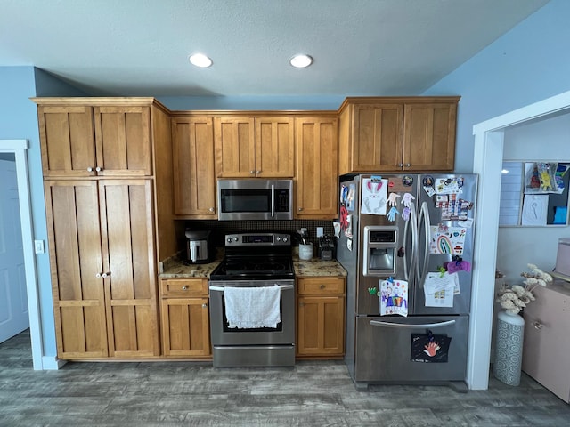 kitchen with dark wood-style floors, recessed lighting, appliances with stainless steel finishes, brown cabinetry, and dark stone counters