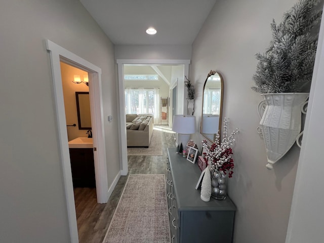 hallway with dark wood-type flooring, a sink, and baseboards