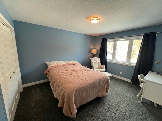 bedroom with a textured ceiling, dark colored carpet, a closet, and baseboards