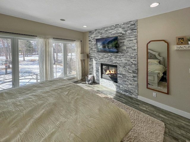 bedroom with a stone fireplace, recessed lighting, wood finished floors, and baseboards