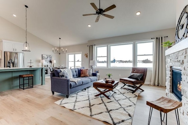 living room with high vaulted ceiling, a stone fireplace, recessed lighting, ceiling fan with notable chandelier, and light wood finished floors