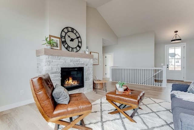 living room featuring high vaulted ceiling, a fireplace, wood finished floors, and baseboards