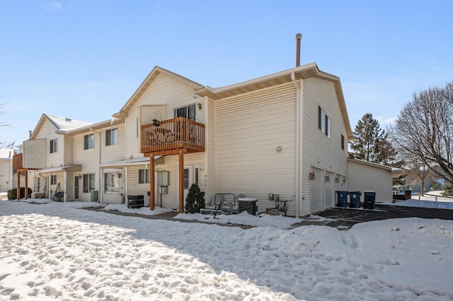 snow covered rear of property with a balcony, an attached garage, and central air condition unit