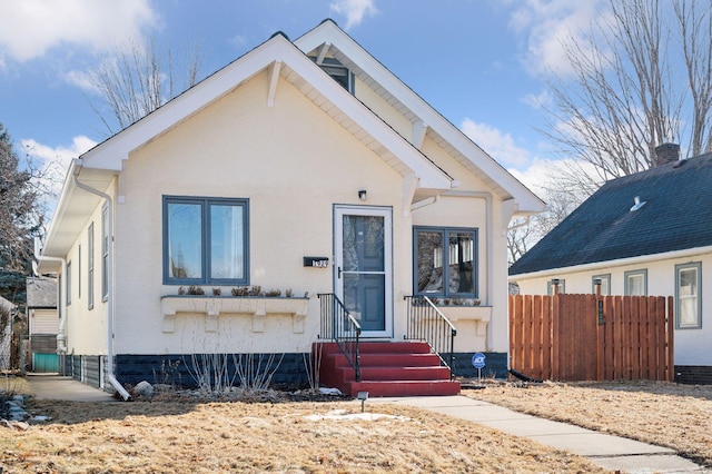 bungalow-style house with entry steps, fence, and stucco siding