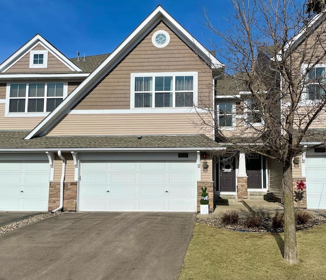 view of front of home with a front yard, a shingled roof, a garage, stone siding, and aphalt driveway