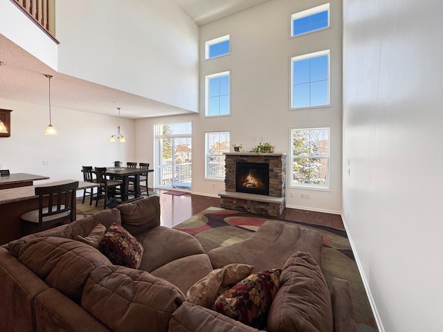 living room with a stone fireplace, wood finished floors, baseboards, and a towering ceiling