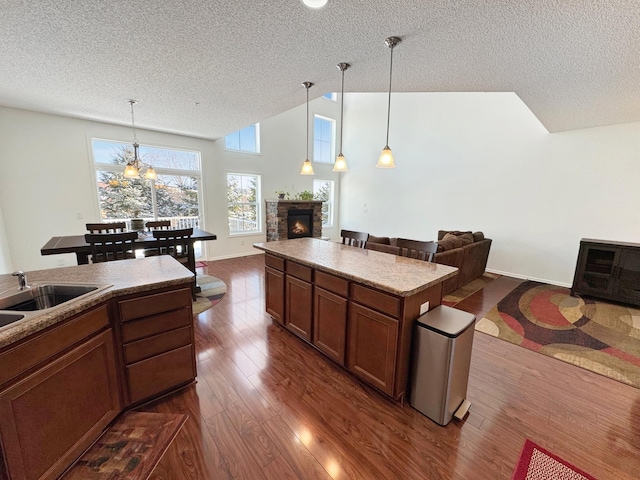 kitchen featuring pendant lighting, a stone fireplace, open floor plan, and dark wood-style flooring