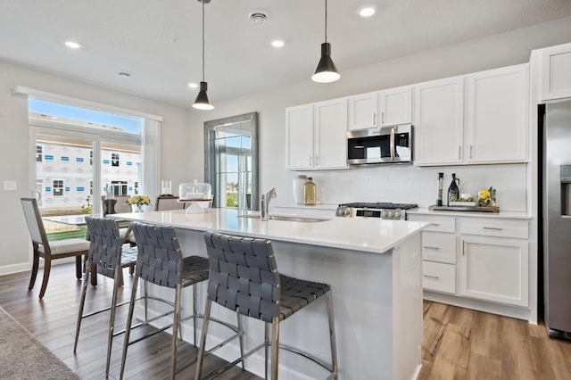 kitchen featuring hanging light fixtures, appliances with stainless steel finishes, a kitchen island with sink, white cabinets, and a sink