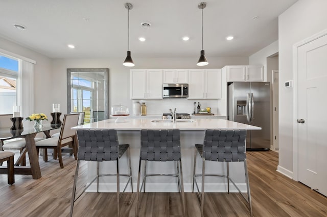 kitchen with a center island with sink, light countertops, hanging light fixtures, appliances with stainless steel finishes, and white cabinetry