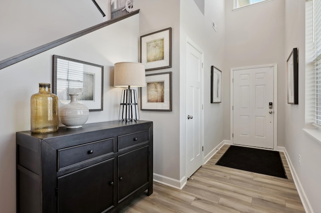 doorway to outside featuring light wood-style floors, a towering ceiling, and baseboards