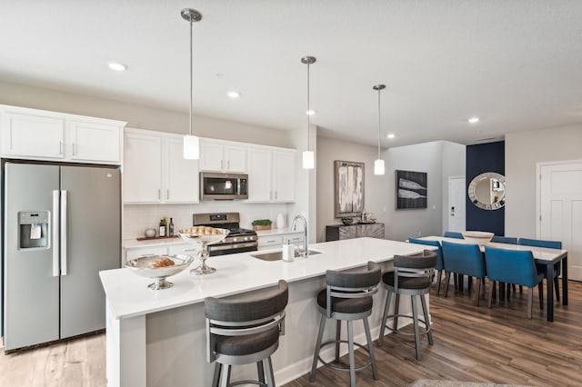 kitchen featuring a kitchen island with sink, a sink, light countertops, appliances with stainless steel finishes, and decorative light fixtures