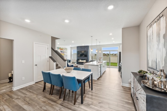 dining area with light wood-type flooring, a large fireplace, stairway, and baseboards