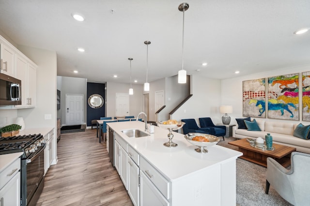 kitchen featuring a center island with sink, open floor plan, stainless steel appliances, light countertops, and a sink