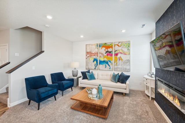 living area featuring carpet floors, visible vents, baseboards, stairway, and a glass covered fireplace