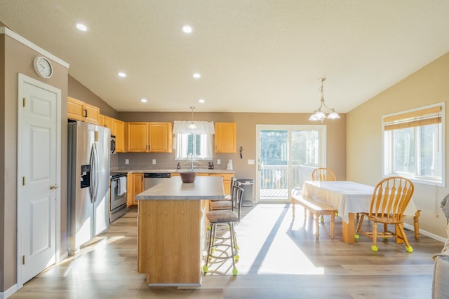 kitchen with pendant lighting, a breakfast bar area, appliances with stainless steel finishes, a kitchen island, and vaulted ceiling