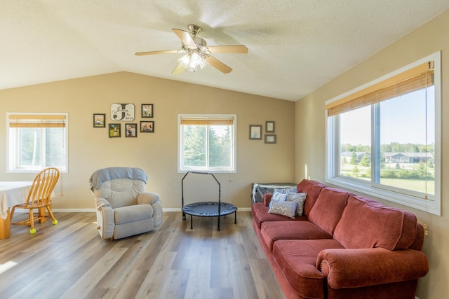 living room featuring lofted ceiling, light wood-style floors, a ceiling fan, a textured ceiling, and baseboards