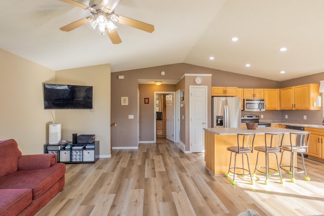 kitchen with stainless steel appliances, light countertops, open floor plan, a kitchen island, and a kitchen bar