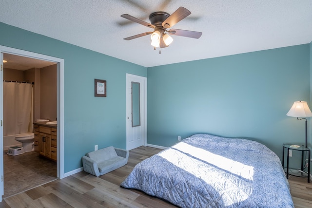 bedroom with baseboards, connected bathroom, ceiling fan, a textured ceiling, and light wood-type flooring