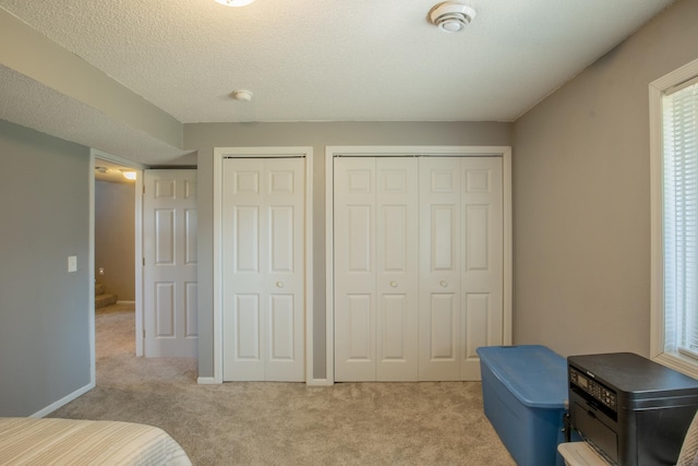 bedroom with light carpet, a textured ceiling, baseboards, and multiple closets