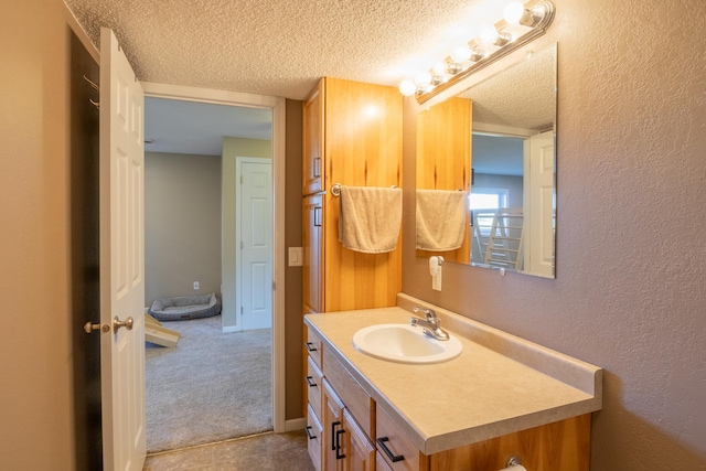 bathroom featuring a textured ceiling, a textured wall, and vanity