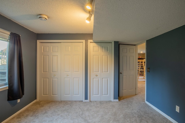 unfurnished bedroom featuring a textured ceiling, baseboards, light colored carpet, and multiple closets