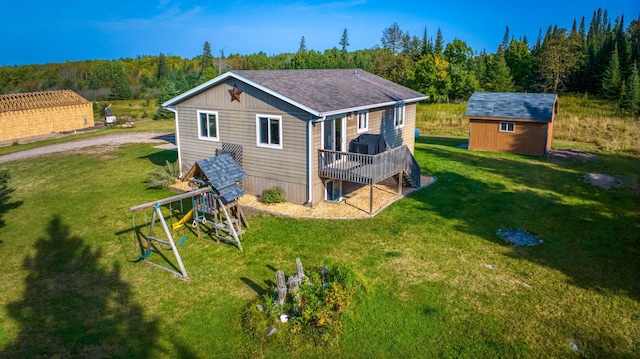 back of house with an outbuilding, a playground, a storage shed, a lawn, and a view of trees