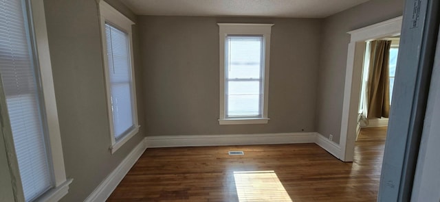 unfurnished room with a textured ceiling, dark wood-style flooring, visible vents, and baseboards