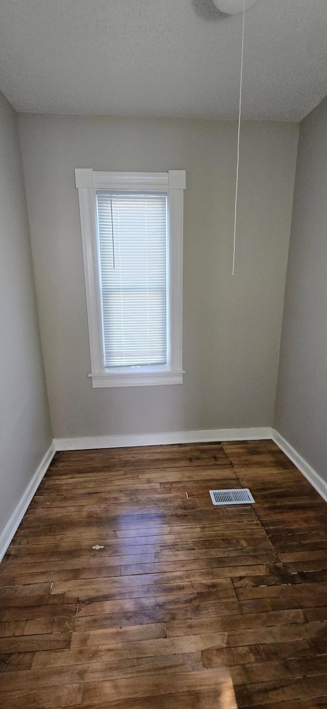 unfurnished room with dark wood-style floors, attic access, visible vents, and baseboards