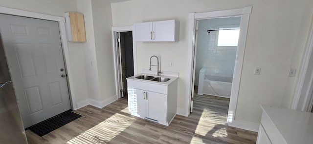 kitchen with a sink, baseboards, white cabinets, light countertops, and light wood-type flooring