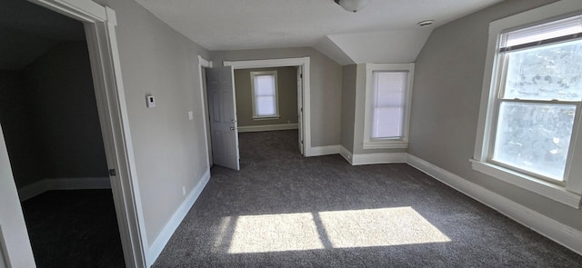 bonus room with lofted ceiling, dark colored carpet, and baseboards