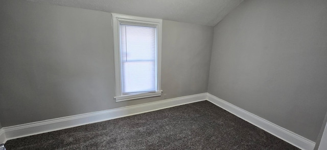 empty room with a textured ceiling, carpet floors, lofted ceiling, and baseboards