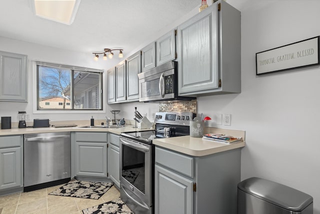 kitchen featuring gray cabinetry, a sink, stainless steel appliances, light countertops, and decorative backsplash