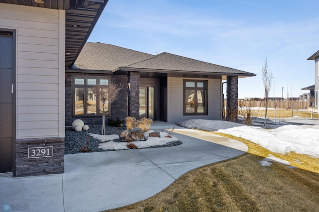 property entrance with stone siding, a shingled roof, and fence