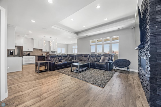 living area featuring a tray ceiling, a fireplace, recessed lighting, light wood-type flooring, and baseboards