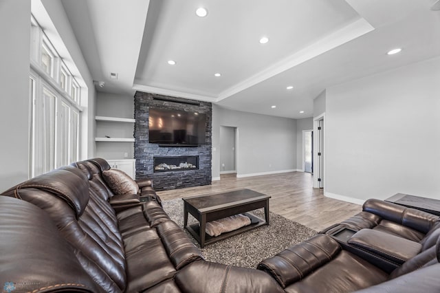 living room featuring a tray ceiling, a fireplace, recessed lighting, light wood-style flooring, and baseboards