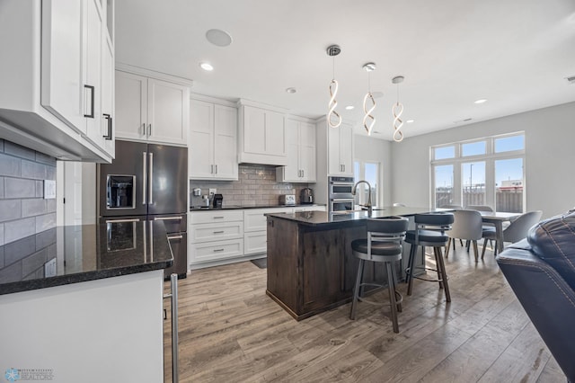 kitchen with stainless steel appliances, white cabinets, a kitchen breakfast bar, backsplash, and light wood finished floors