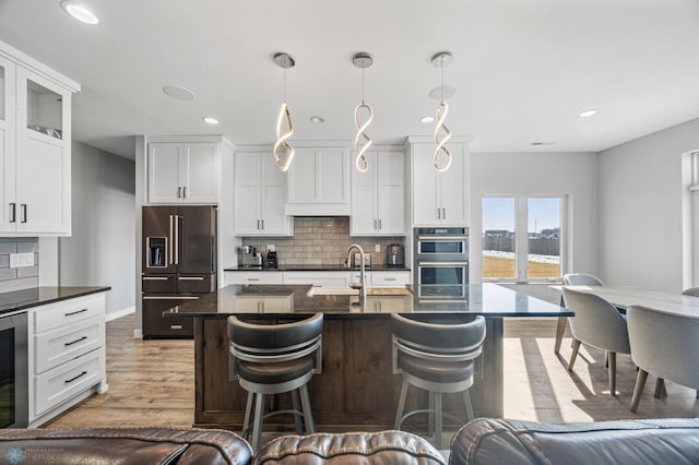 kitchen featuring light wood-style flooring, decorative backsplash, white cabinetry, high end black refrigerator, and a kitchen breakfast bar