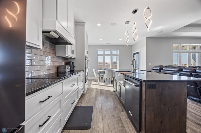 kitchen with stainless steel appliances, open floor plan, backsplash, dark stone counters, and hardwood / wood-style floors