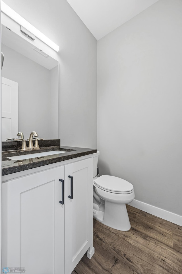 half bath featuring baseboards, vanity, toilet, and wood finished floors