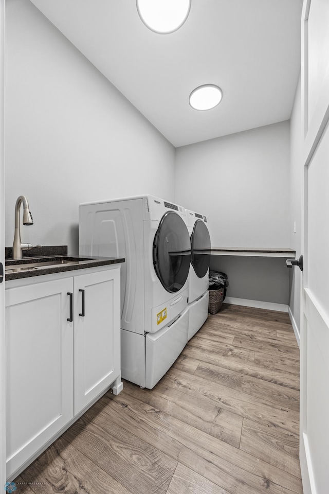 laundry area featuring light wood finished floors, cabinet space, baseboards, washing machine and dryer, and a sink